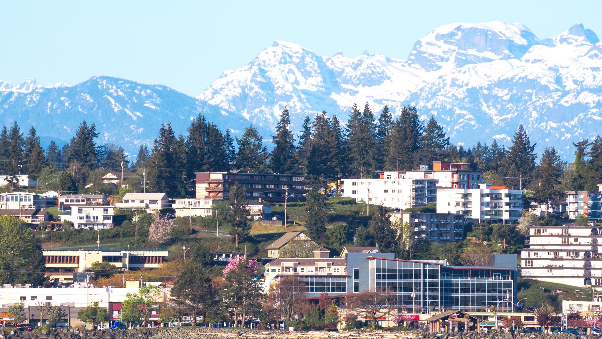 Campbell River viewed from Discovery Passage. Houses, buildings, and trees line the shore with snow-capped mountains in the background.