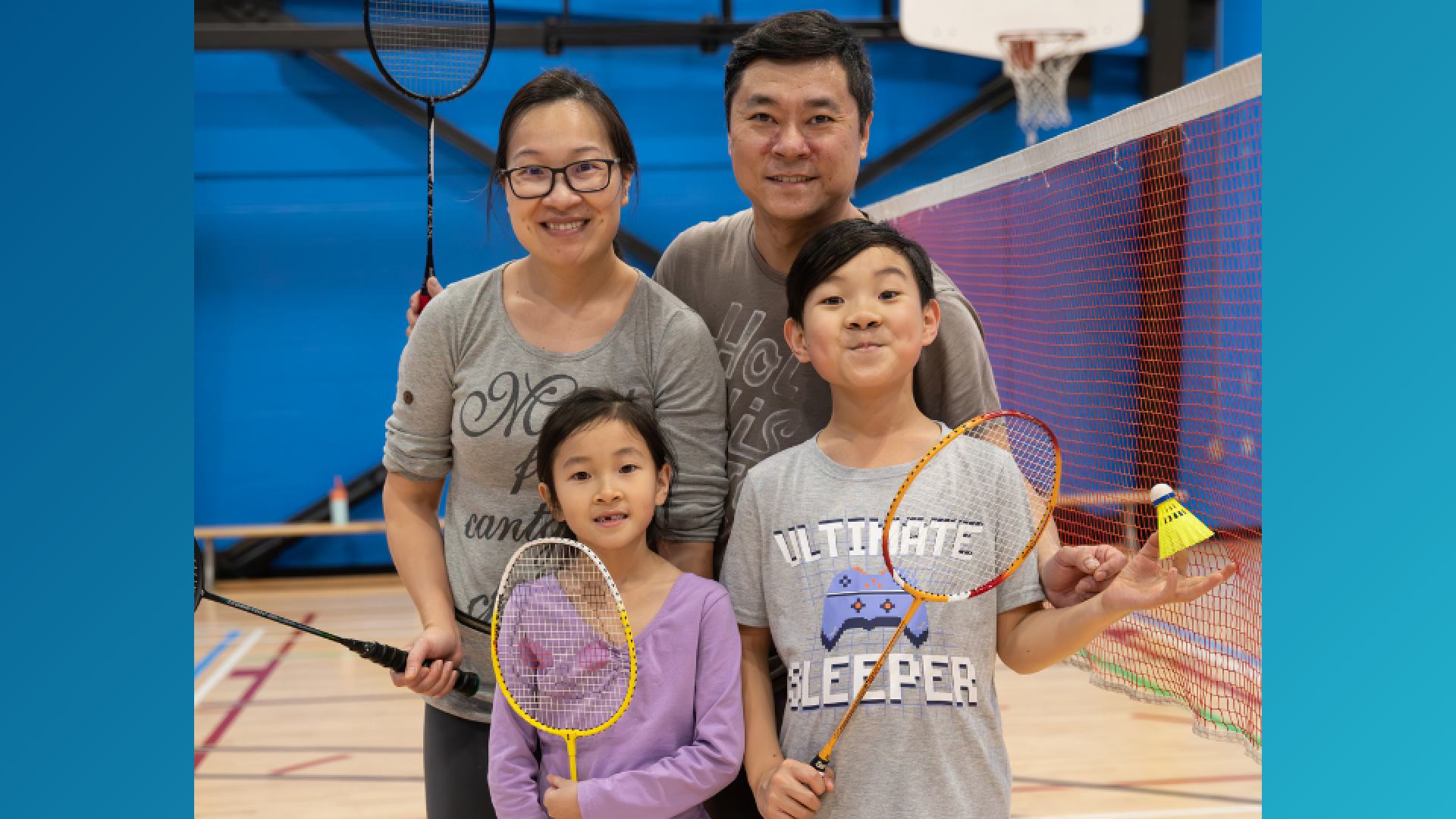 A family of four holding badminton rackets smiling in front of a net.