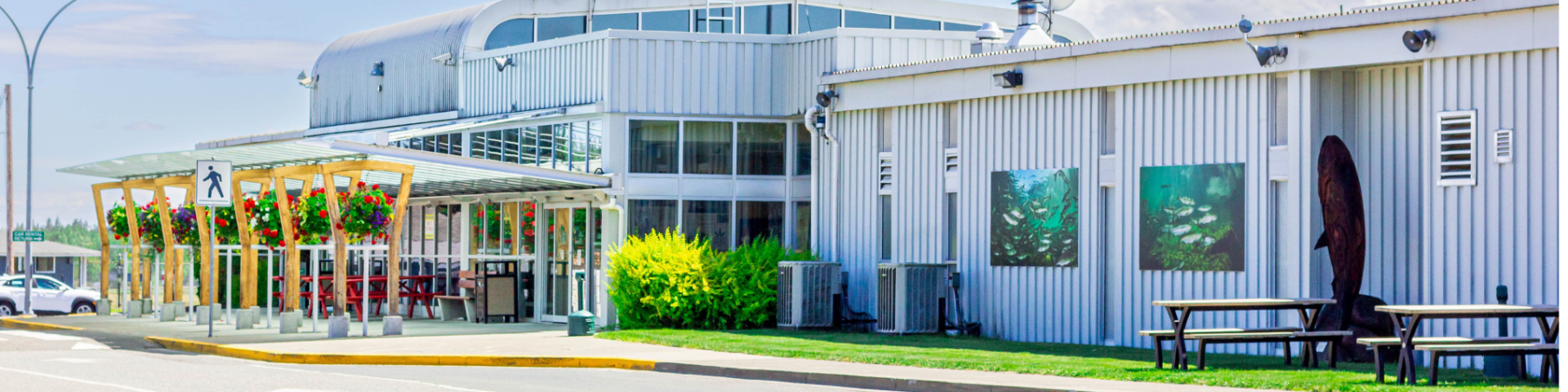 The front of Campbell River Airport with hanging flower baskets and art work of salmon on the front walls