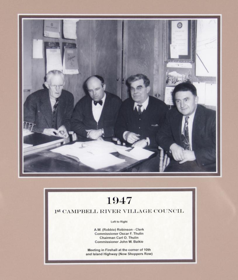 Black and white photo of four men in suits sitting at a table in 1947.