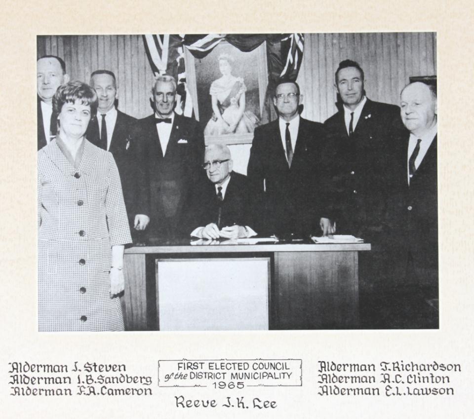 Eight people in suits standing around a desk, black-and-white photo.