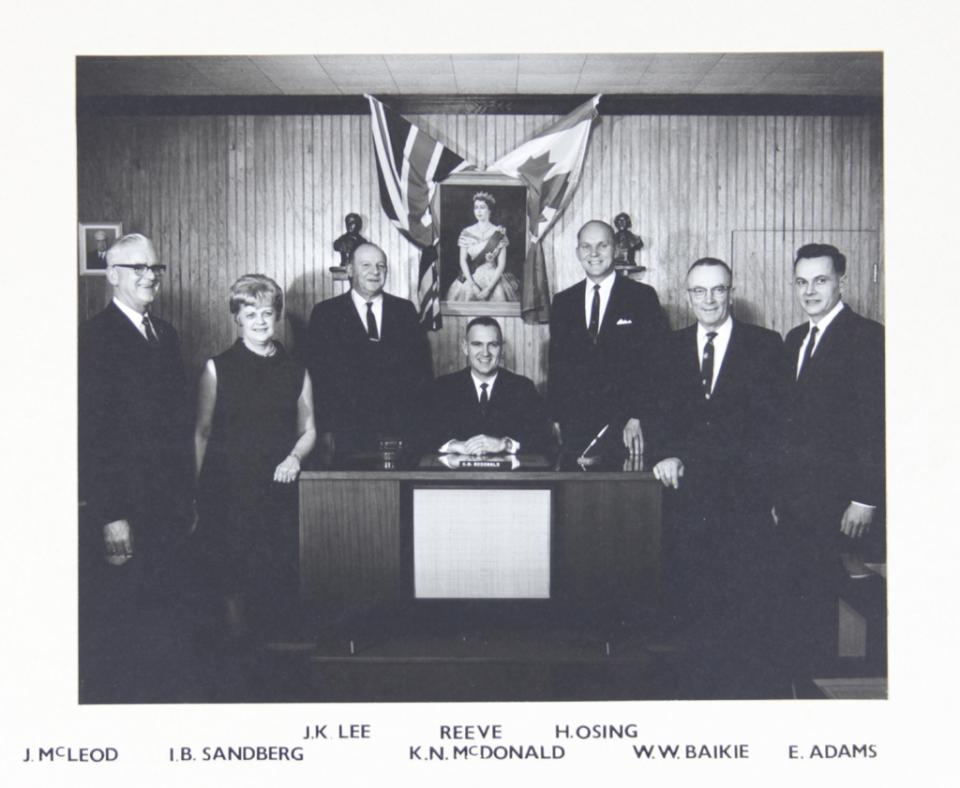 Black and white photo of seven formally dressed adults posed indoors.