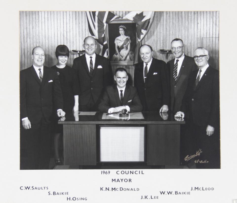 Black and white photo of seven council members posing, one seated at a desk.