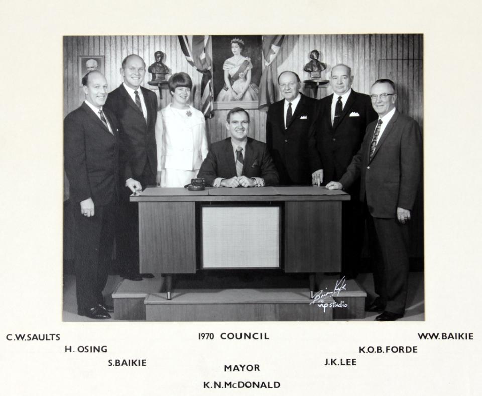 Black and white photo of a mayor with council members, one woman among men, in formal attire.