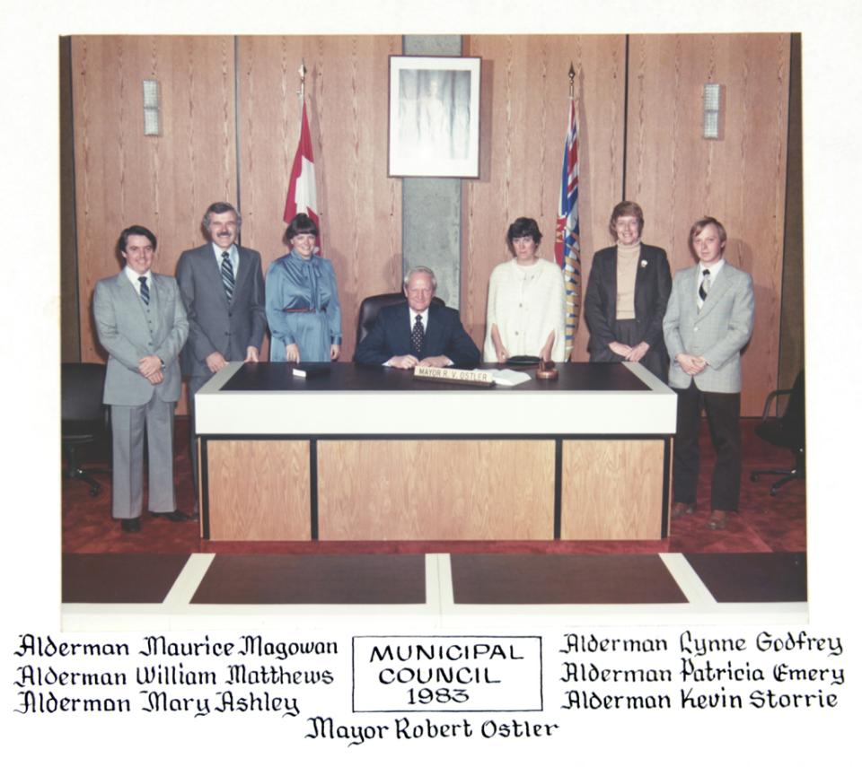 Mayor and six council members pose around a desk in a formal setting.