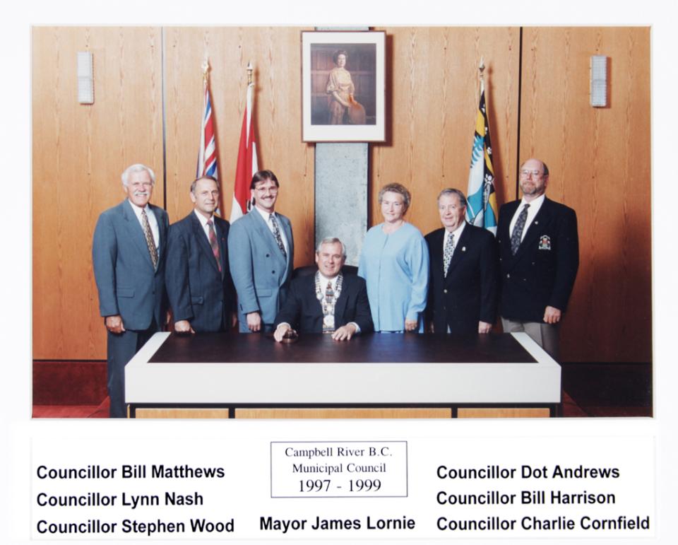 Group photo of officials in formal attire, seated and standing by a table with flags.