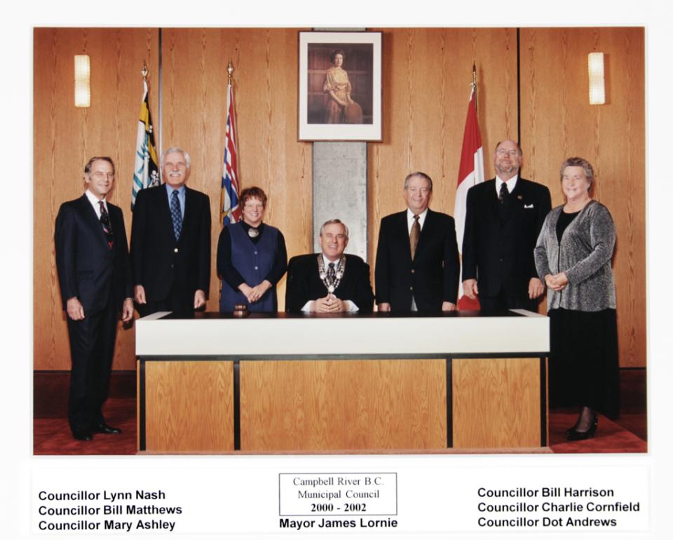 City council members pose in formal attire at a large wooden desk.