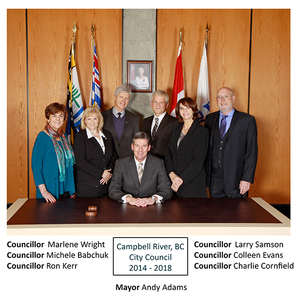 Group of seven people in formal attire, sitting and standing in front of flags.