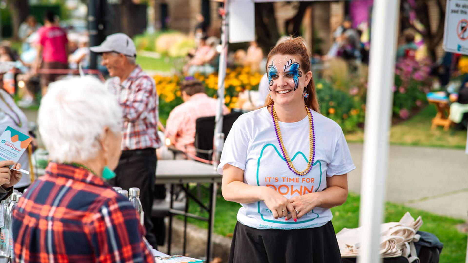 Young woman with butterfly face paint smiling at a community event booth.