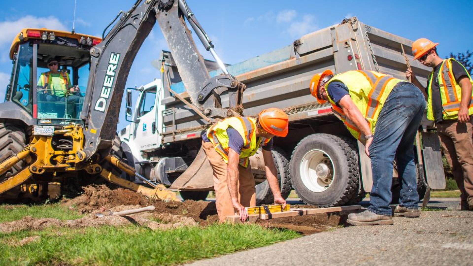 Contruction workers and trucks digging up road.