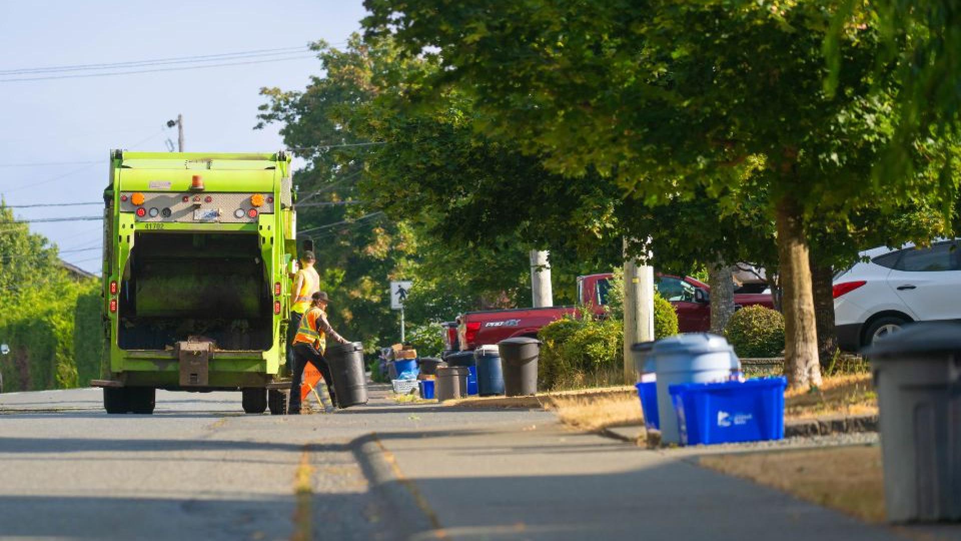 back of a garbage truck with workers grabbing recycling bins.