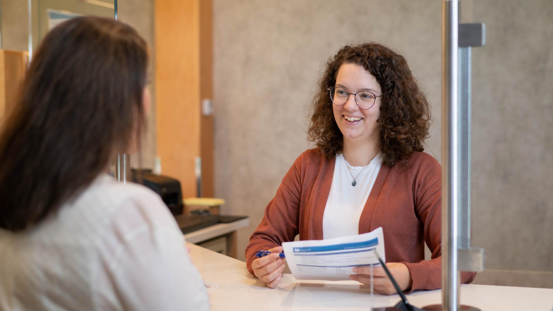 Development Services person smiling at a customer at the counter holding a paper and pen.