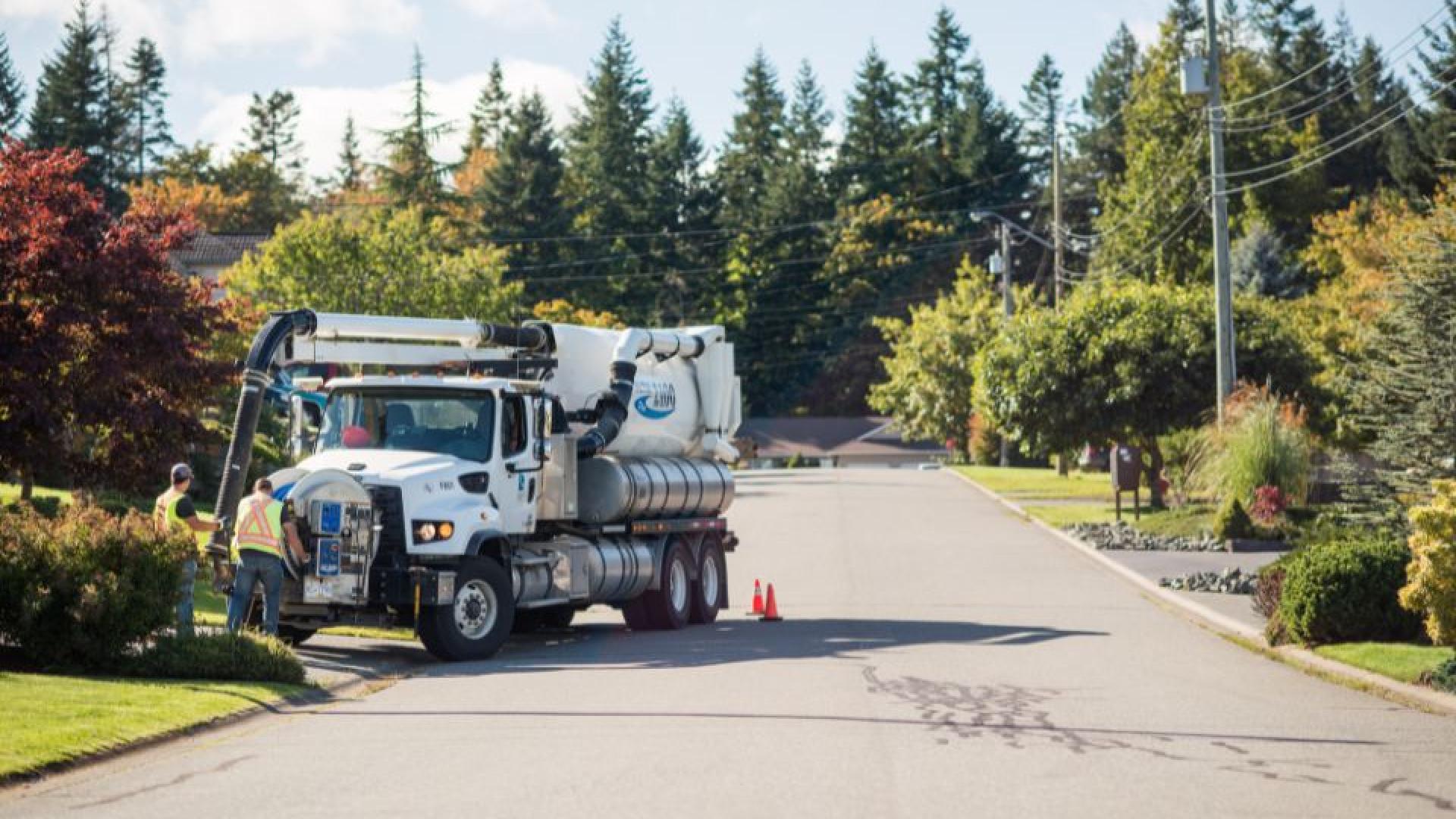 sewer truck doing maintenance on a city street with two workers assisting.