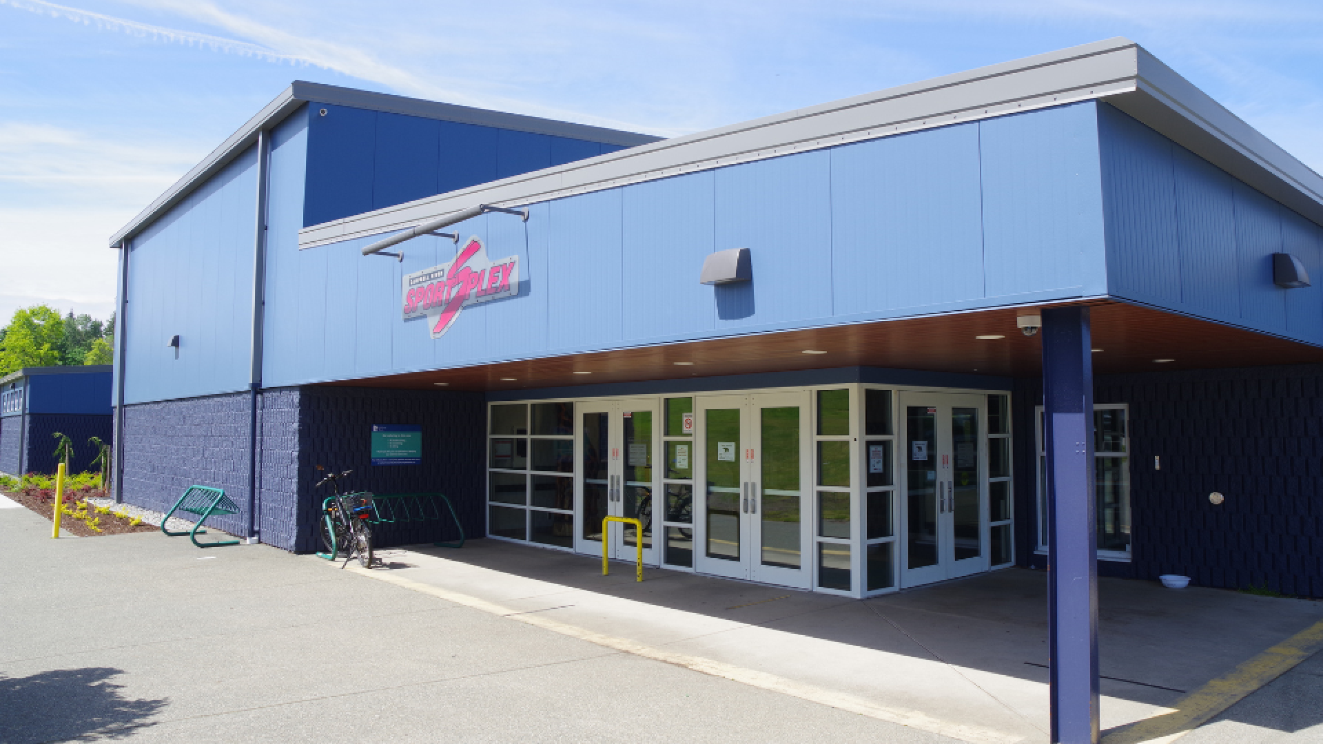 Entrance to the Sportsplex building with a bicycle parked in a nearby bike rack.