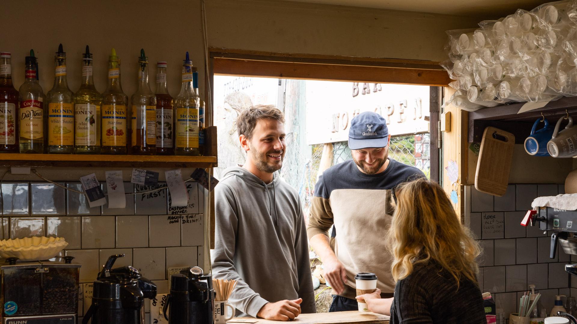 View from inside a food truck looking out as two patrons receive their order from an owner.