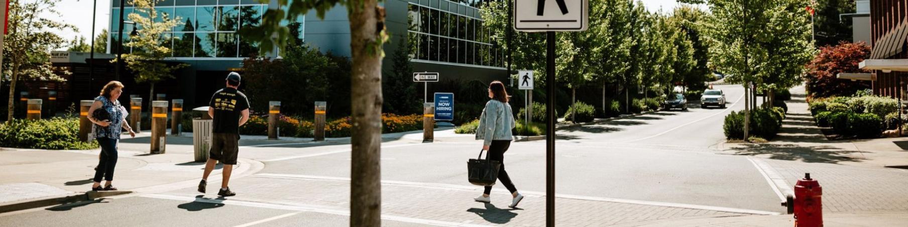 Several people walking across a city street at a crosswalk, with tall buildings lining the background.