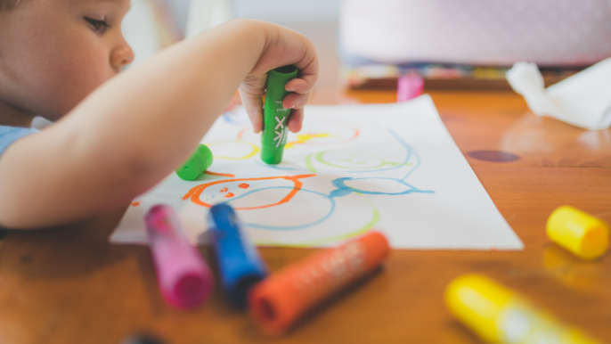 child sitting at a table drawing with markers on a white piece of paper.